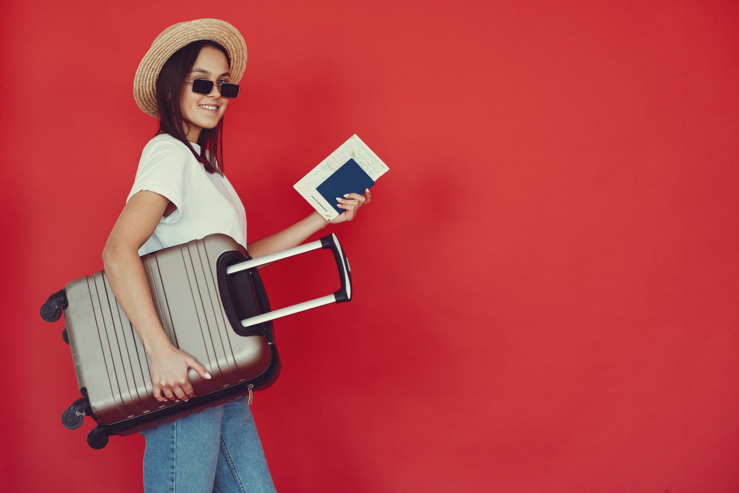 Happy female traveler with suitcase on red background